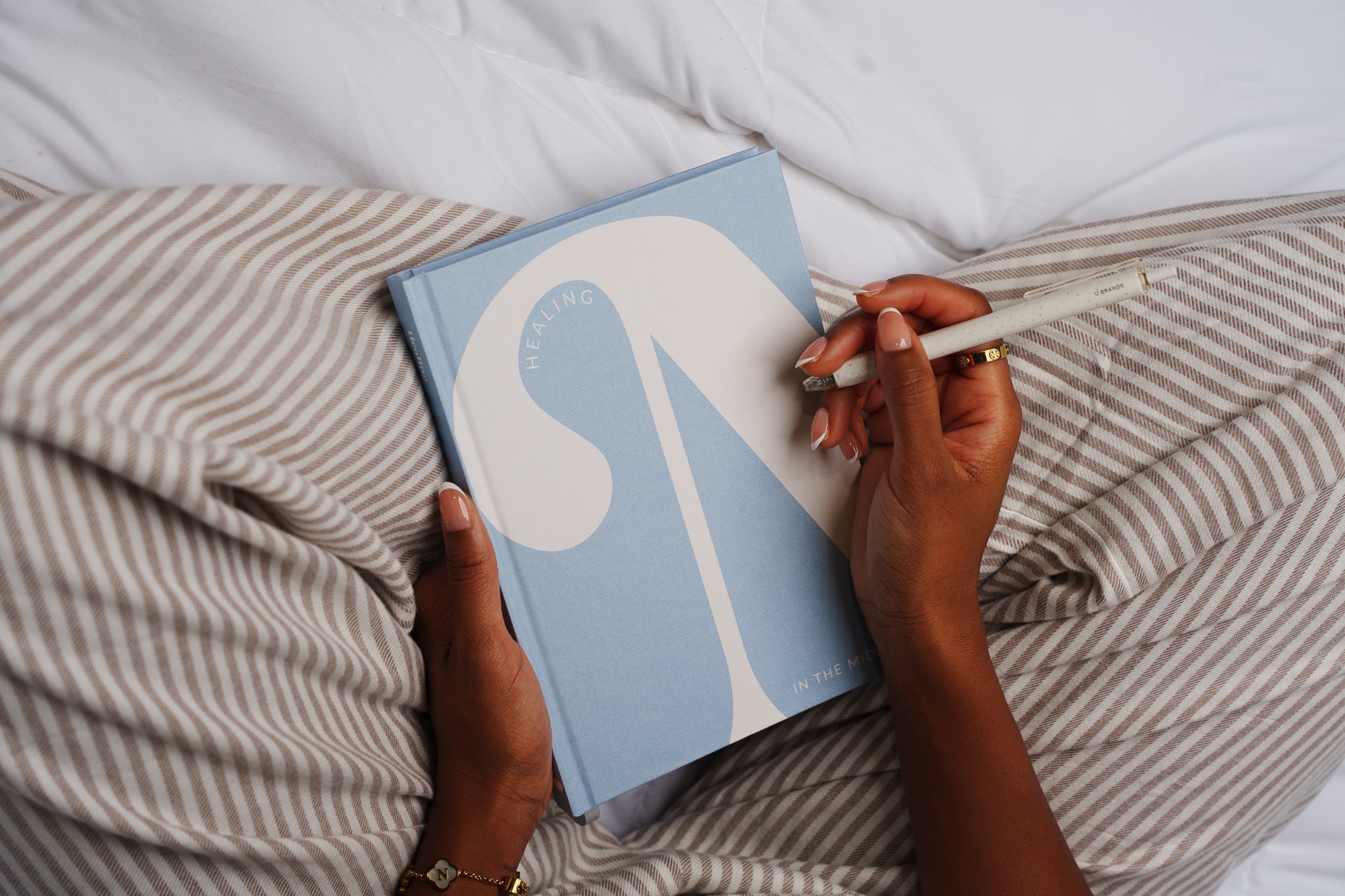 Person holding a blue notebook with a white logo and a pen, sitting on a striped cushion.